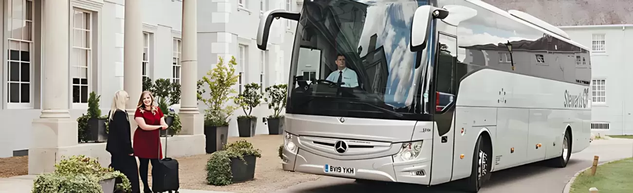 A Stewarts luxury coach parked outside a hotel building with two women and luggage near the entrance.